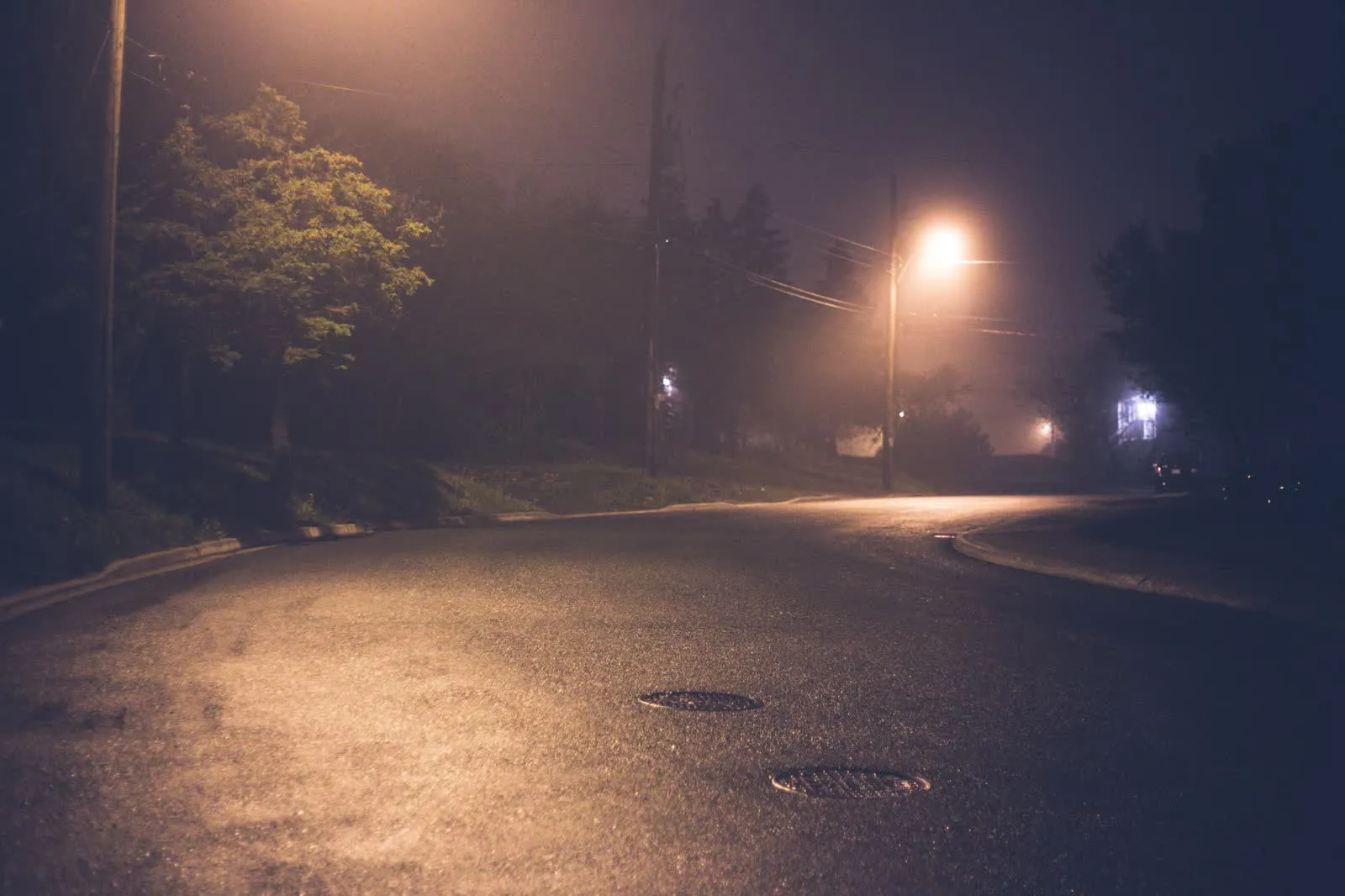 A quiet suburban street lit by streetlights on a foggy night.