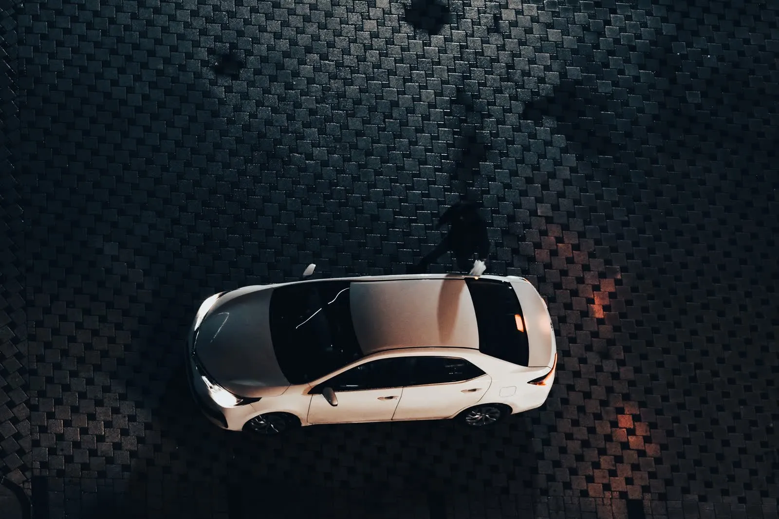 A car parked alone on a dark street at night, seen from above.