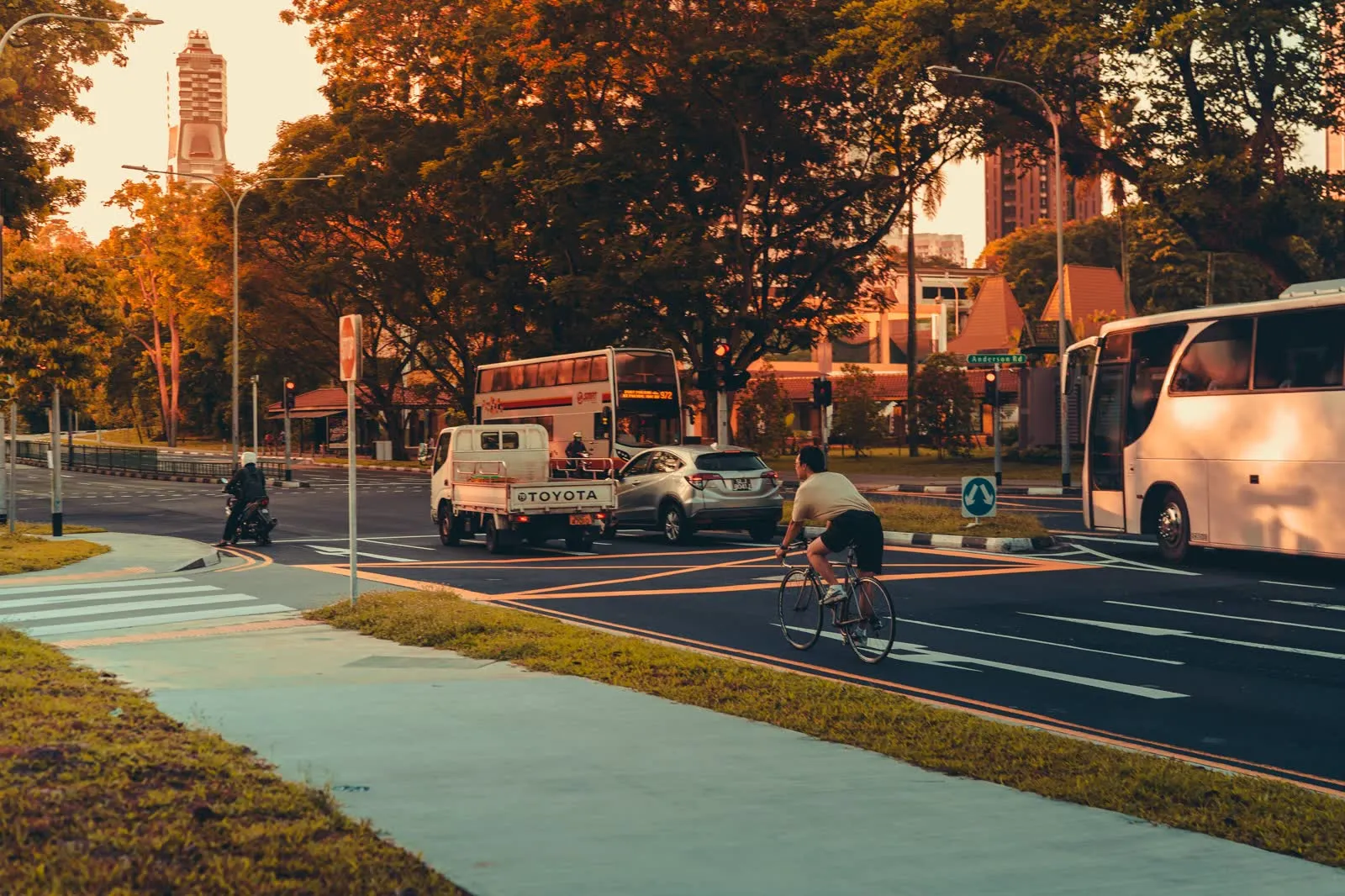A cyclist riding on a city road alongside traffic in the early morning.